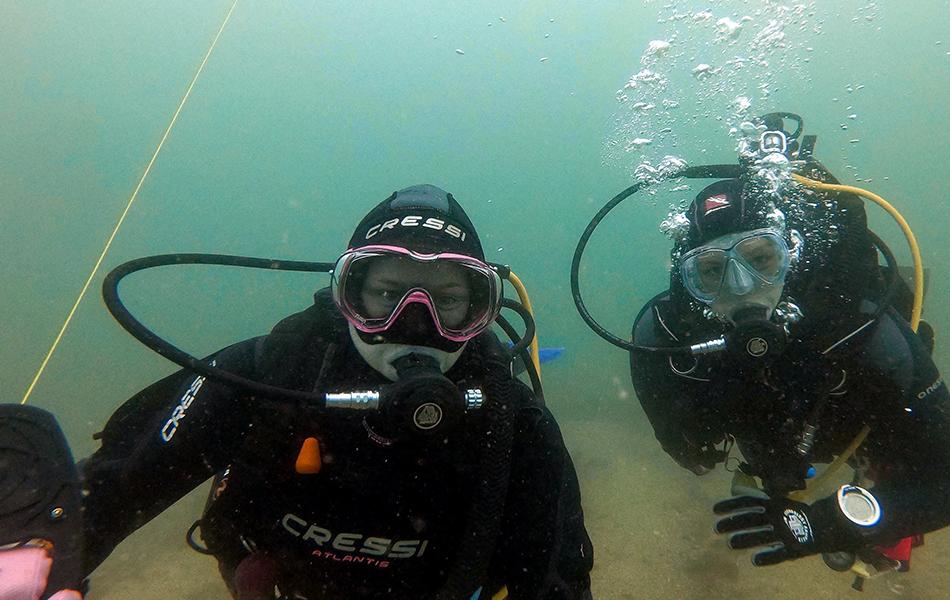 A diver with a reel and their buddy looking at the camera