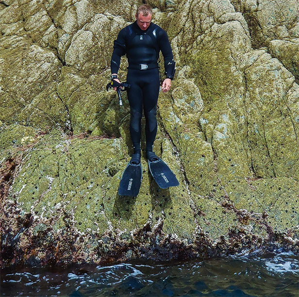 Andy Torbet in wetsuit and fins observing a river from the rocky bank
